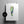 A vertical art print featuring a watercolor-style image of Pine Valley hole 5. Fairway illustration in green, blue, and beige tones, hanging against a light gray wall with two black binder clips. A black circular badge on the left reads 'TURN YOUR MOMENT INTO ART.