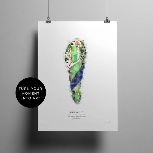 A vertical art print featuring a watercolor-style image of Pine Valley hole 5. Fairway illustration in green, blue, and beige tones, hanging against a light gray wall with two black binder clips. A black circular badge on the left reads 'TURN YOUR MOMENT INTO ART.